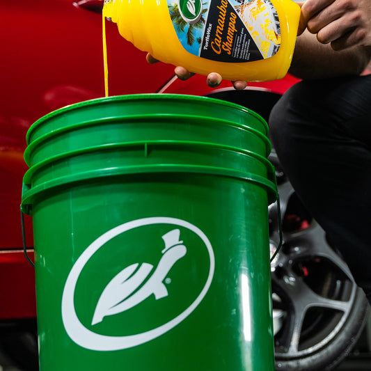 Pouring Turtle Wax Carnauba Shampoo into a bucket. The green bucket has a running turtle on it.