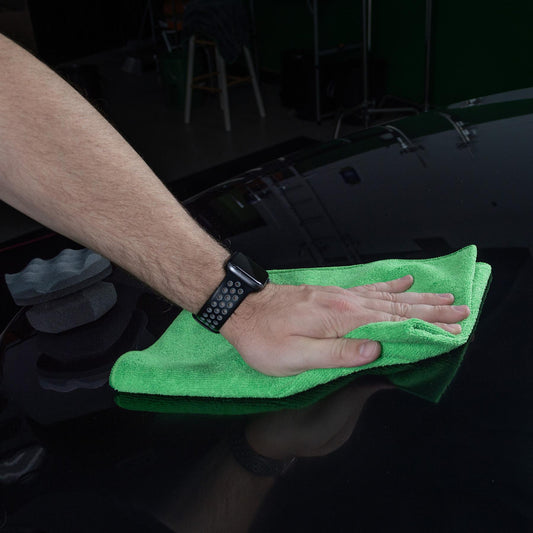 Man polishing a black car with a bright green microfibre cloth. Car care, detailing and automotive.