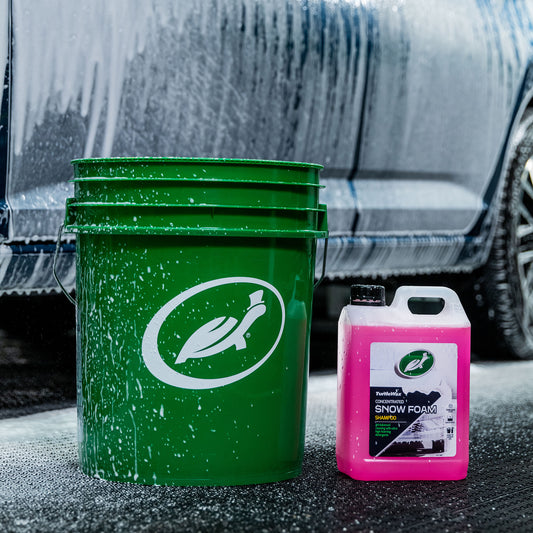 Turtle Wax cleaning combo: bucket with logo and pink concentrated Snow Foam shampoo for car cleaning. Vehicle lathered behind.