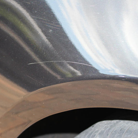 Close-up of a scratched, dark-coloured car panel near a wheel arch. Needs Turtle Wax scratch repair.