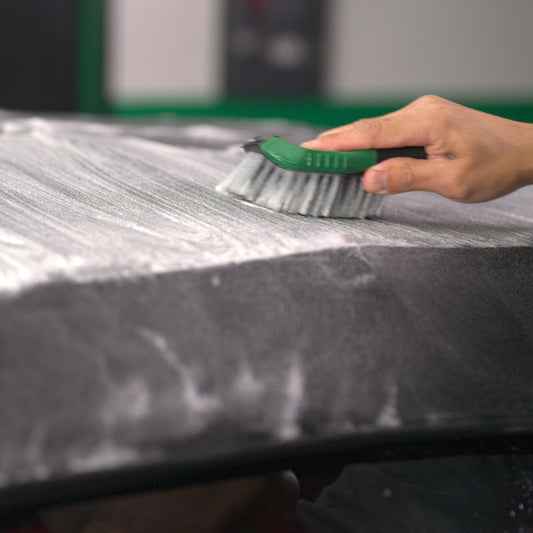 Hand brushing fabric with suds. Automotive detailing using Turtle Wax Hybrid Solutions for stain removal and deep clean.