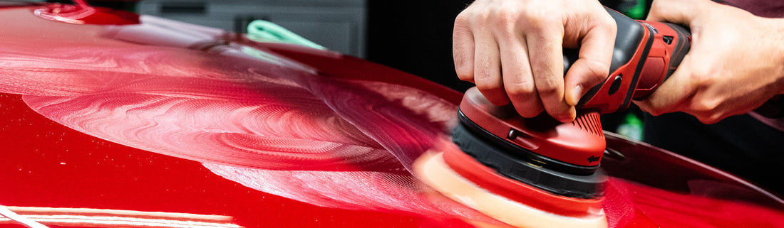 Man using a polishing machine on a red car. 
