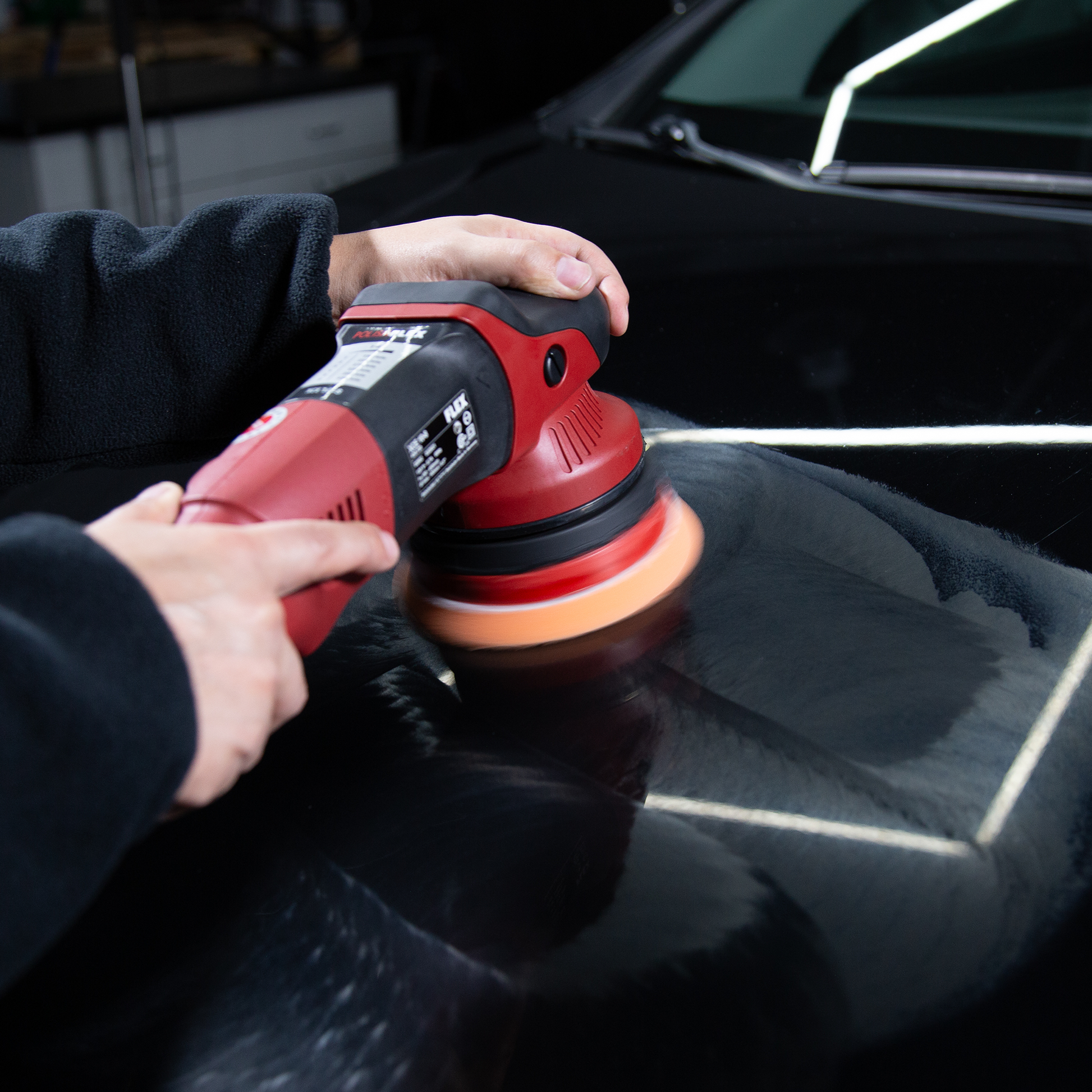 Car detailing: a red polisher refines black car paint, removing swirls. Turtle Wax expertise for a sleek finish.