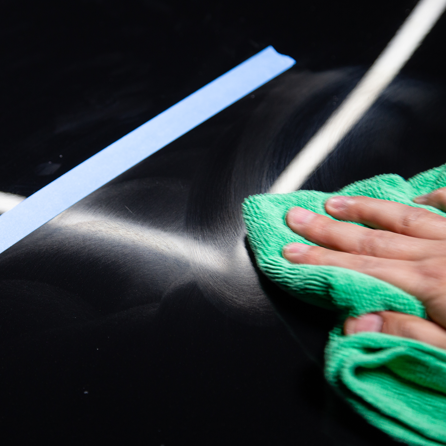 Car detailing in progress: A hand buffing scratches on a black car with a cloth. Repairing vehicle paintwork.