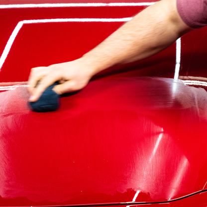 Person using Turtle Wax rubbing compound on red car paintwork to remove scratches.