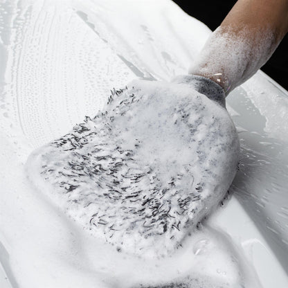 A microfibre wash mitt is covered in foamy soap and is being used to clean a car.