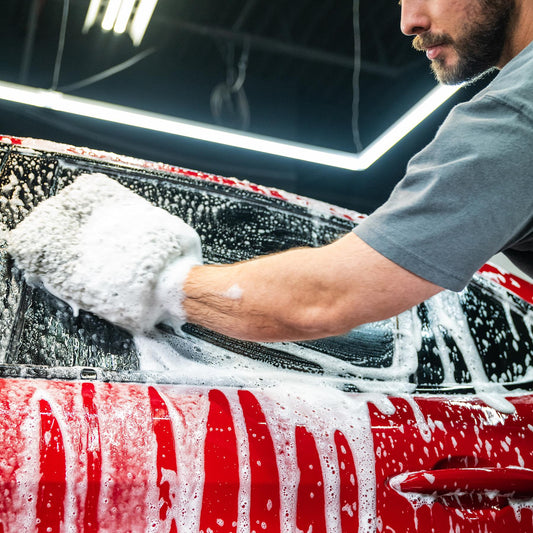 Man washing a red car with a foamy mitt. Car cleaning and detailing.