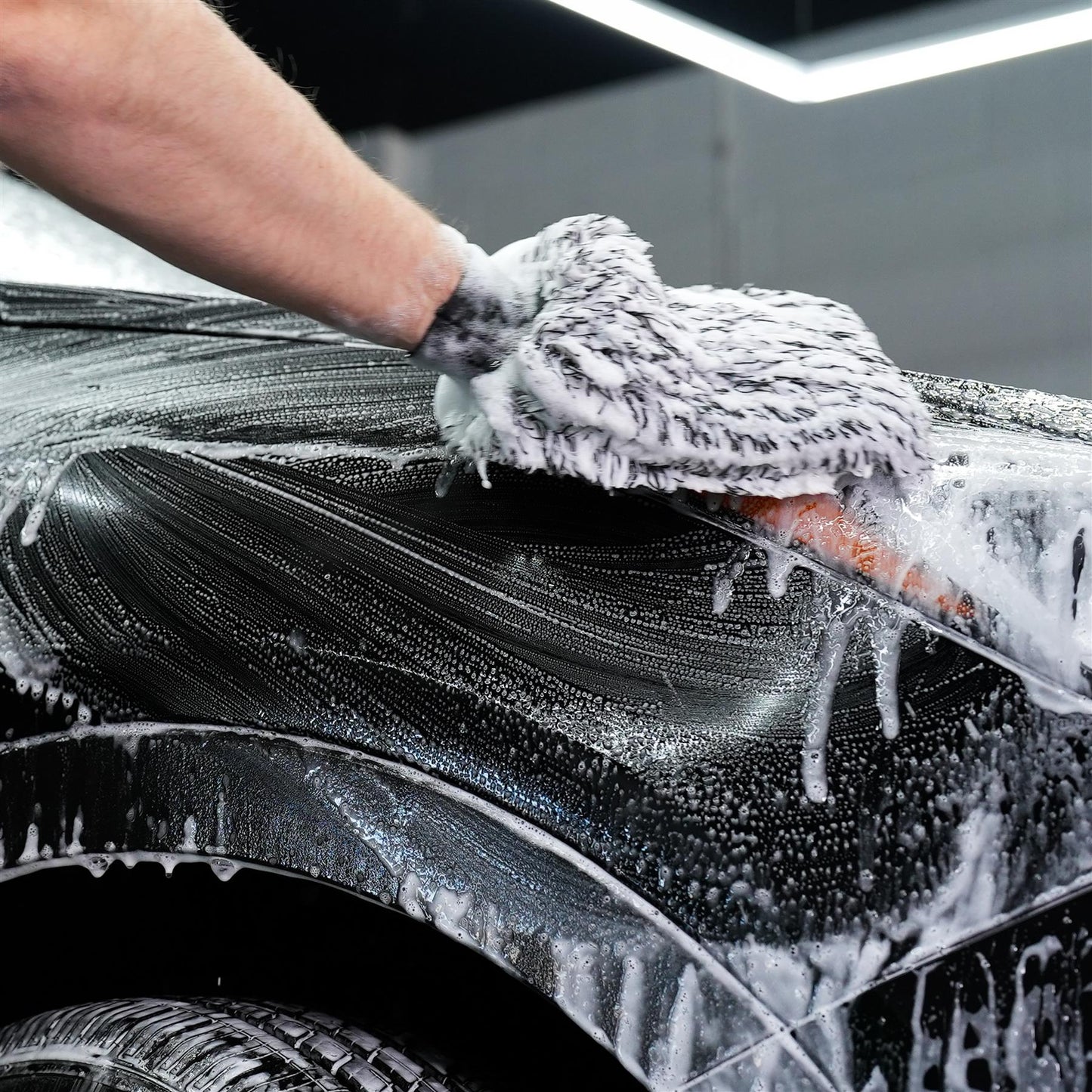 Soapy car wash. Hand cleaning black vehicle bodywork using a mitt. Automotive detailing and valeting service.