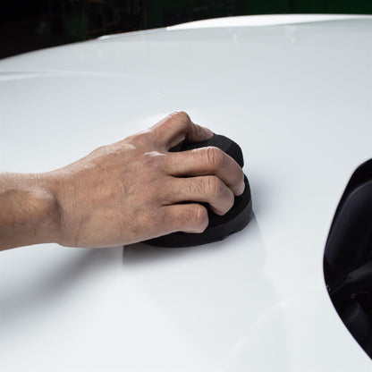 Buffing white auto paintwork. Hand polishing with black foam pad for car detailing.
