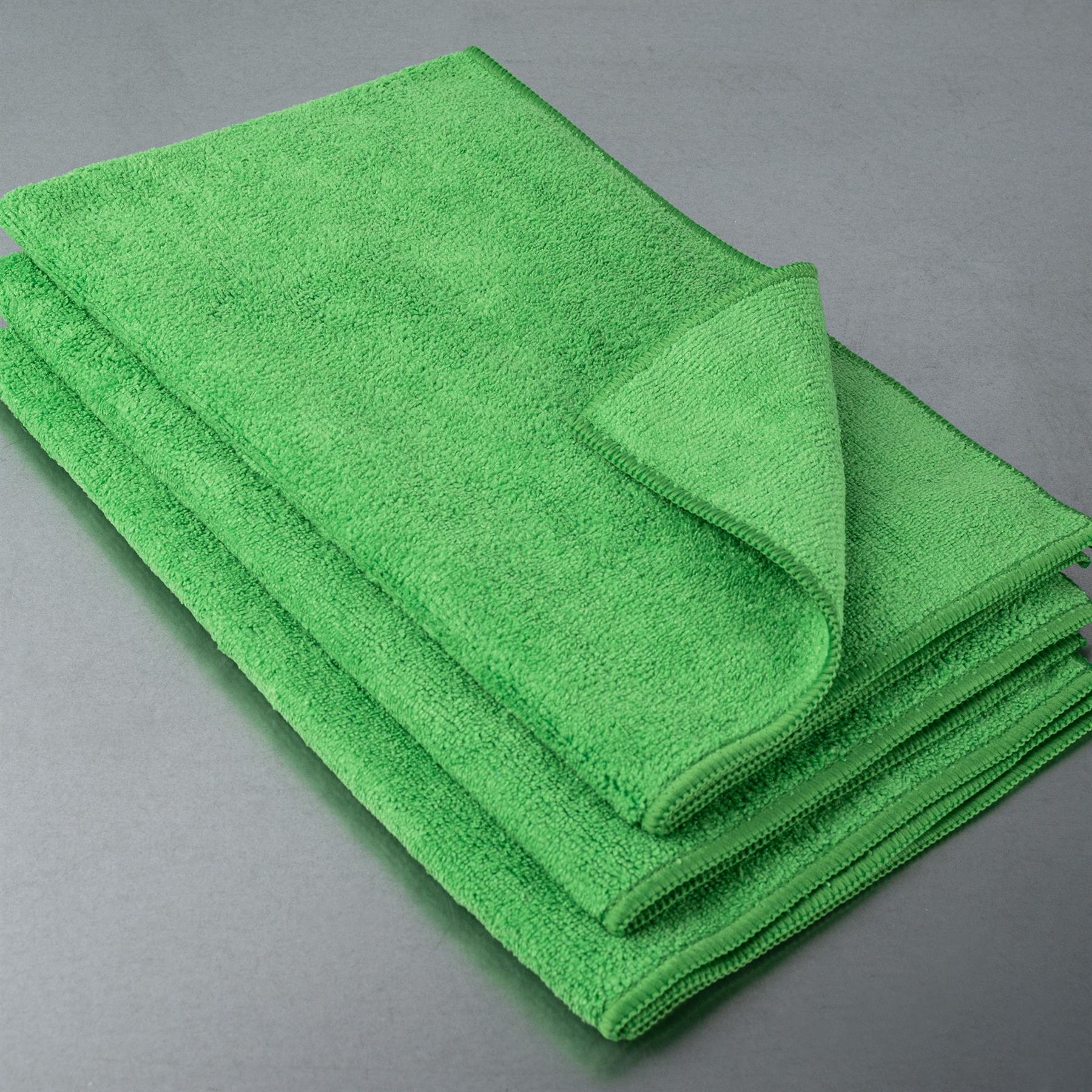 Bright green pile of absorbent cloths. Close-up of stacked cleaning textiles with stitched edges, on a grey surface.
