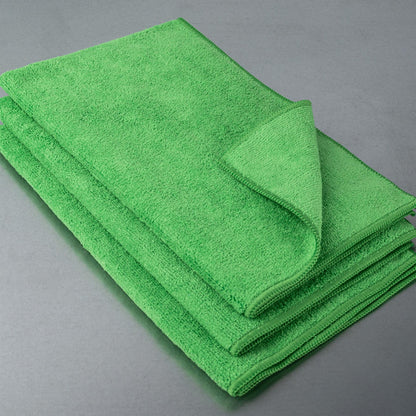 Bright green pile of absorbent cloths. Close-up of stacked cleaning textiles with stitched edges, on a grey surface.
