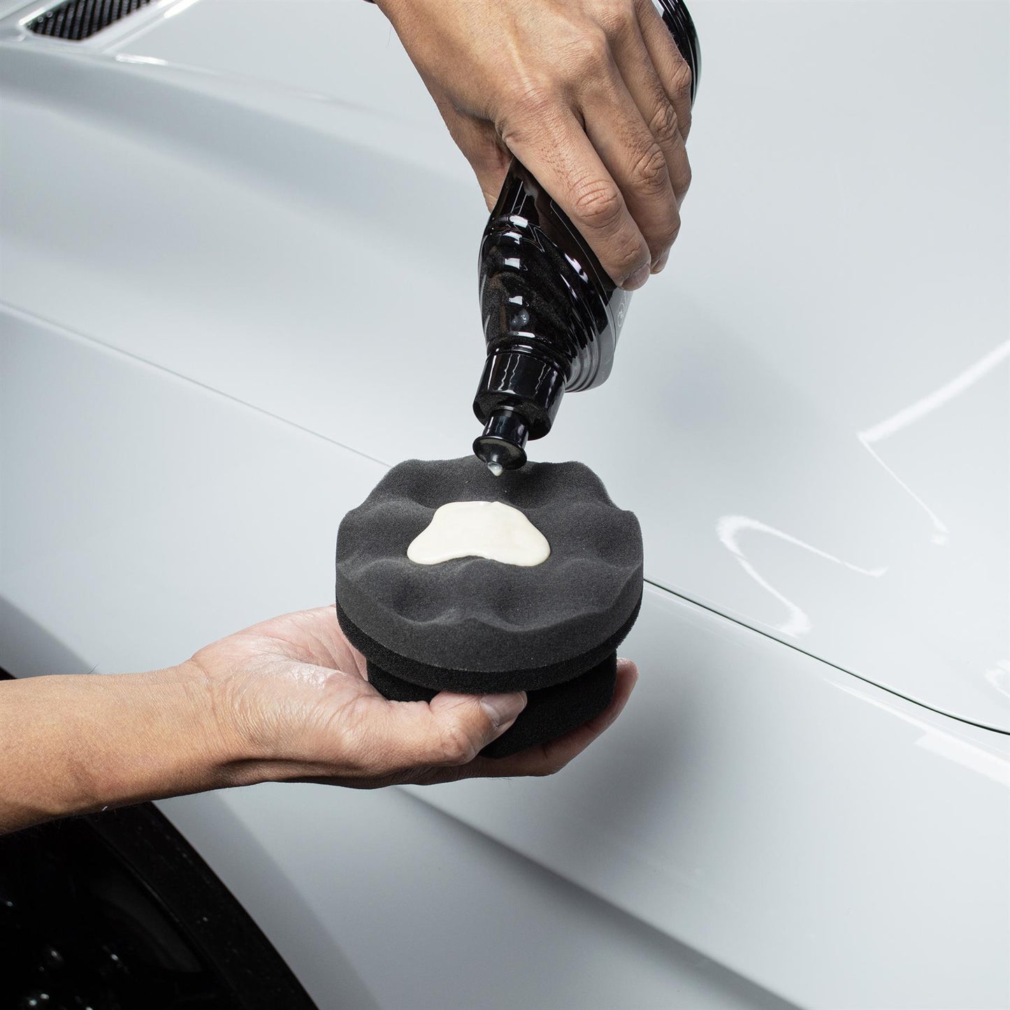 Car detailing prep: Wax being applied to foam applicator pad on vehicle.