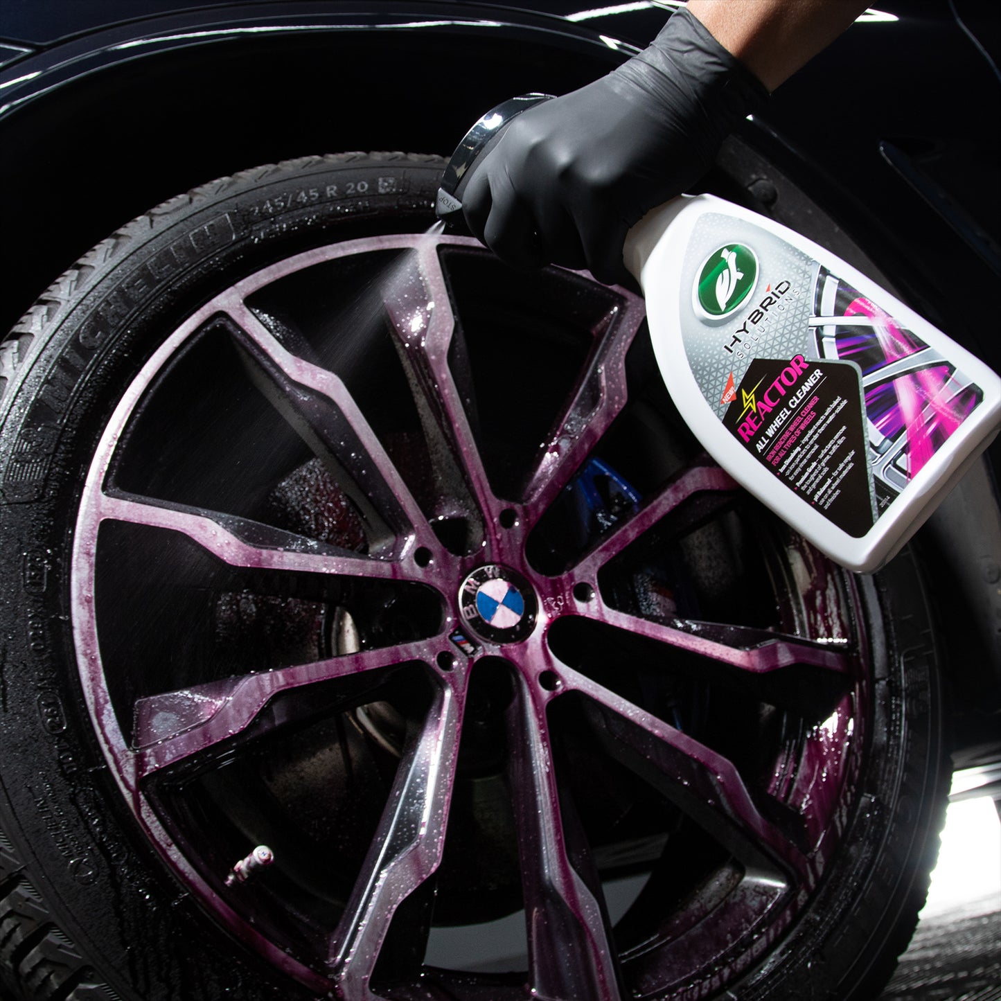 BMW alloy wheel being sprayed with Turtle Wax Hybrid Solutions Reactor cleaner. Purple residue shows reaction with brake dust.