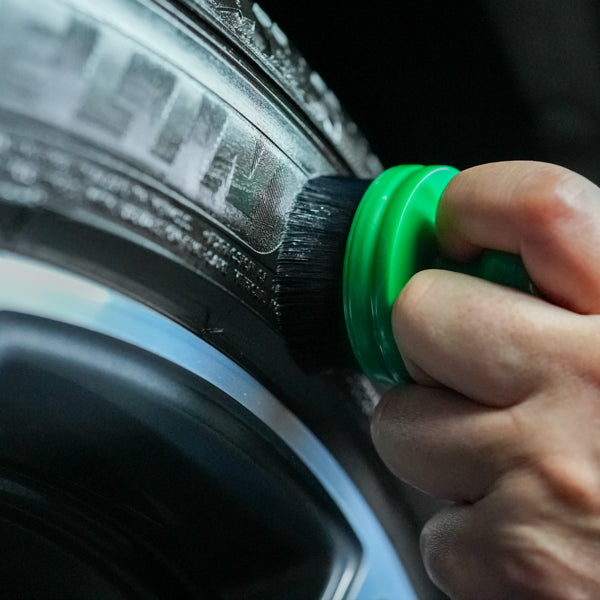 Tyre dressing applicator shown applying to car tyres. Features ergonomic green handle for car detailing or cleaning.