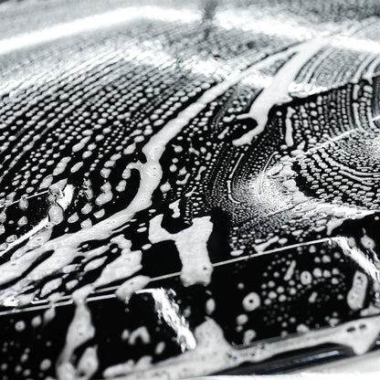 Sudsy car wash closeup. Glossy black paintwork being cleaned with white soap lather. Automotive detailing.