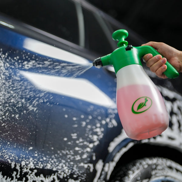 Turtle Wax foaming sprayer in use. Hand holds the green and white pressure sprayer, applying foam to a blue car. Car detailing.