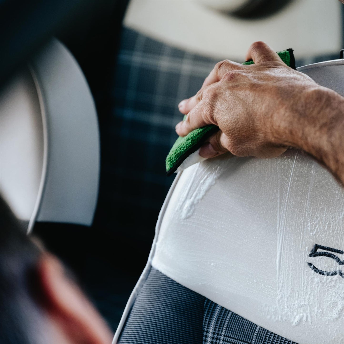 Car interior cleaning: A hand wipes a white door trim with a green microfibre cloth, leaving a streak of cleaning product.