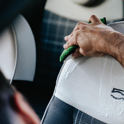 Car interior cleaning: A hand wipes a white door trim with a green microfibre cloth, leaving a streak of cleaning product.