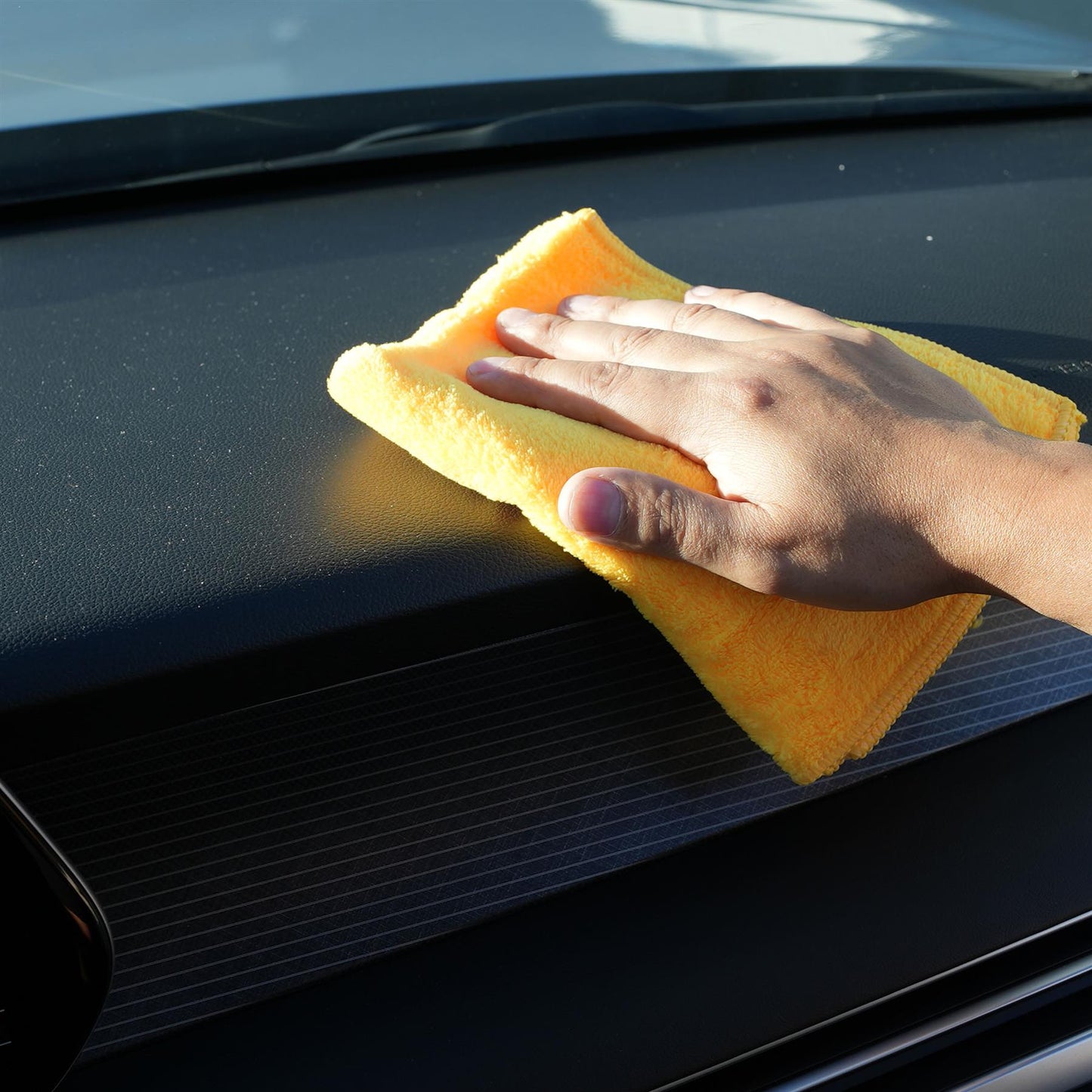 Hand using a yellow microfiber cloth to clean a car's black surface