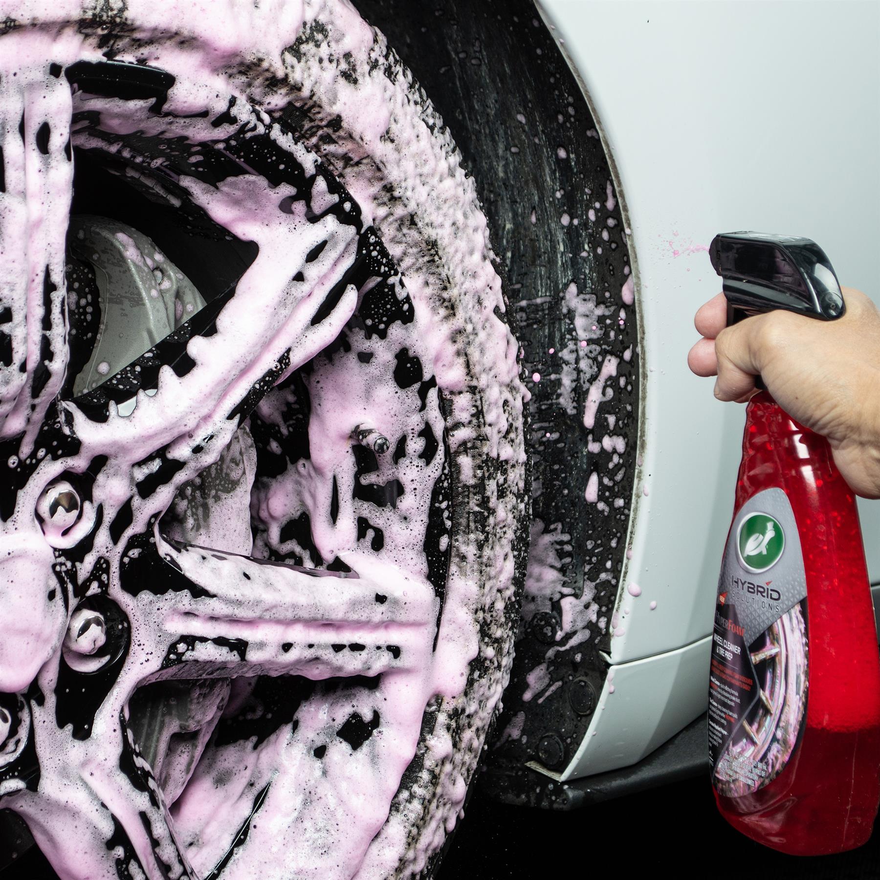 Detailing a black car wheel with Turtle Wax Hybrid Solutions wheel and tyre cleaner. Pink suds cover the wheel, showcasing cleaning power.
