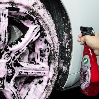 Detailing a black car wheel with Turtle Wax Hybrid Solutions wheel and tyre cleaner. Pink suds cover the wheel, showcasing cleaning power.
