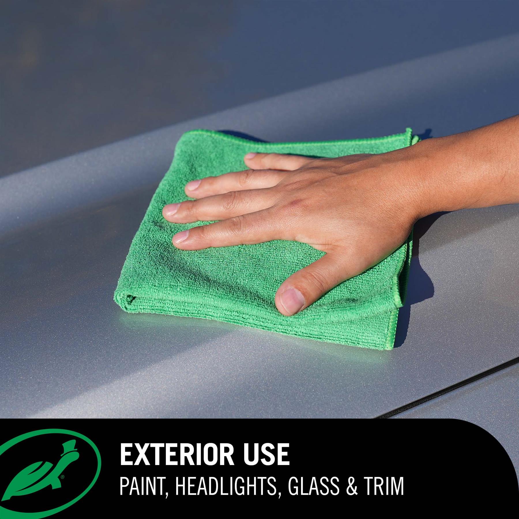 Hand using a green microfiber cloth to clean a car's exterior.