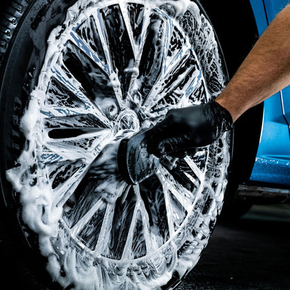 Person cleaning a car wheel with soapy water using a brush