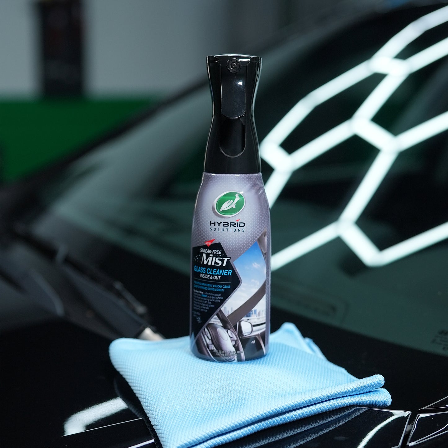 Turtle Wax Hybrid Solutions glass cleaner mist on a car bonnet with a blue cloth. Streak-free formula for inside and outside automotive glass.