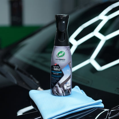 Turtle Wax Hybrid Solutions glass cleaner mist on a car bonnet with a blue cloth. Streak-free formula for inside and outside automotive glass.
