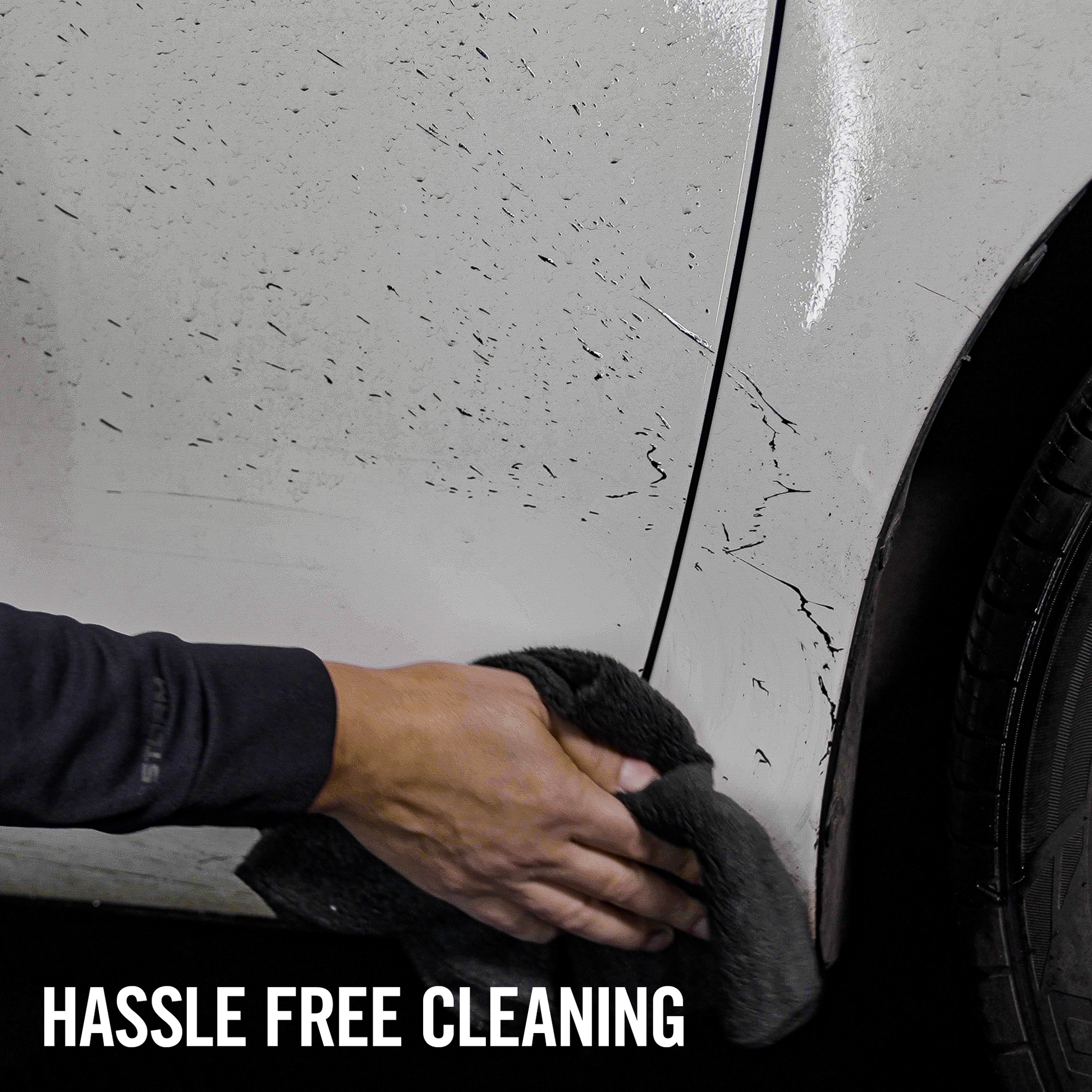 Cleaning car with a cloth. Vehicle bodywork shows residue being removed near wheel arch.
