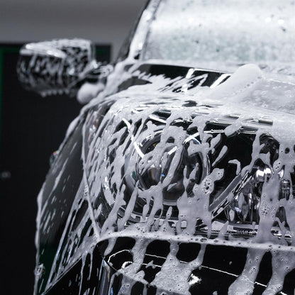 Dark car headlight covered in cleaning foam. Car detailing or valeting.
