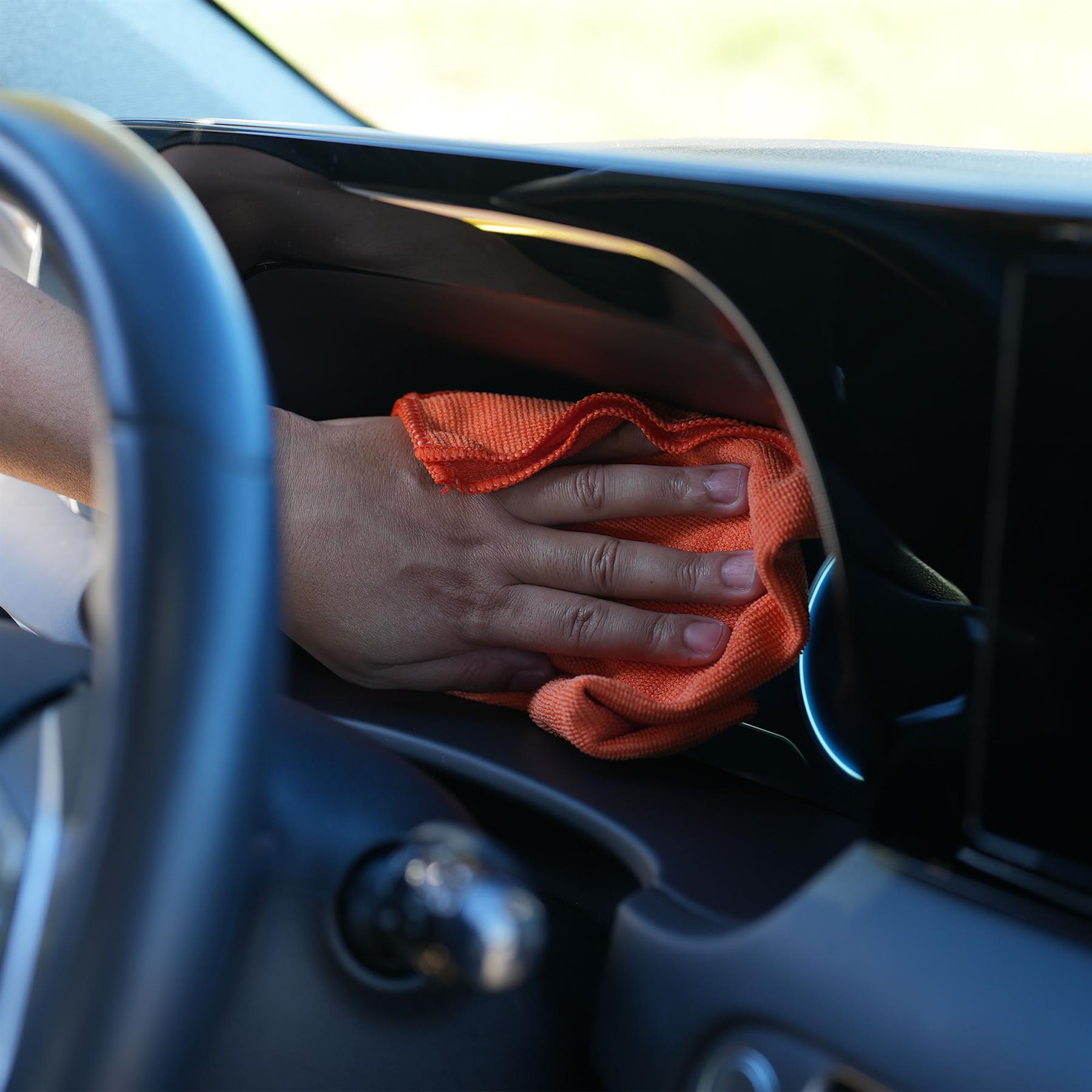 Person cleaning car interior with an orange microfibre cloth