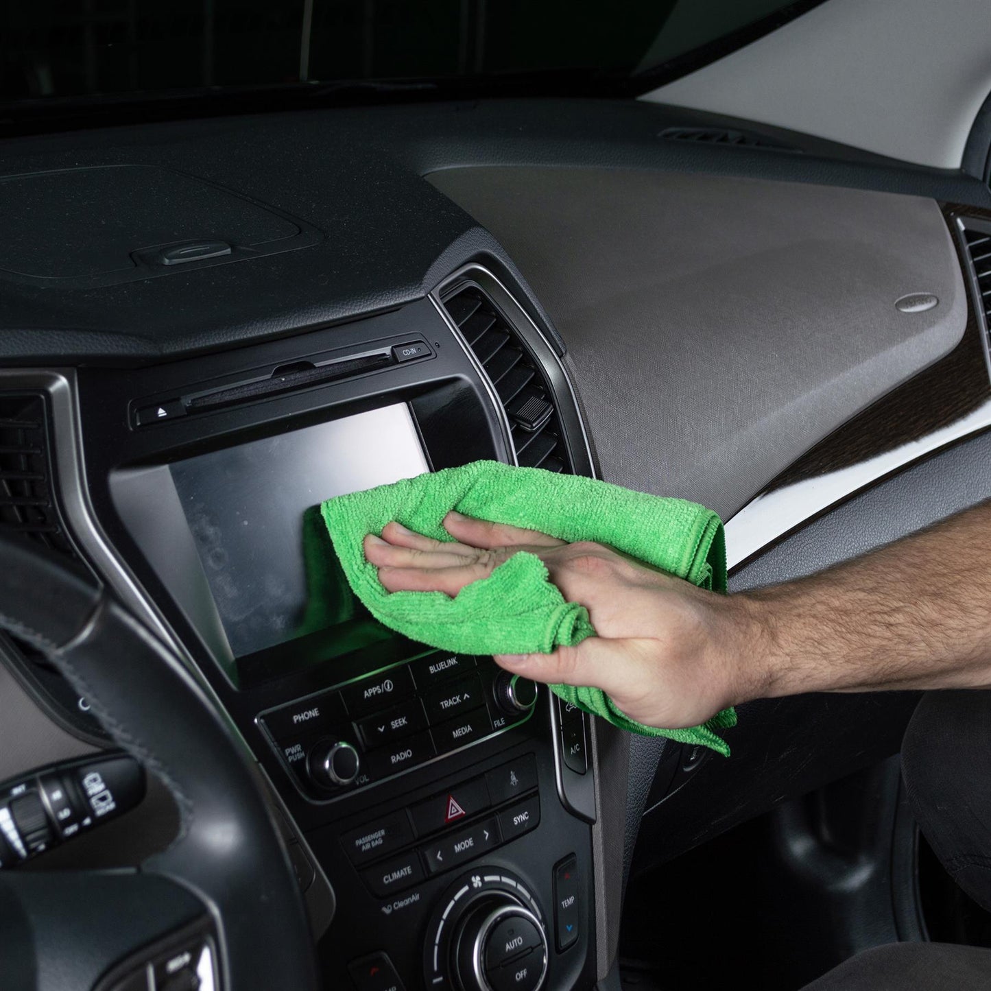 Green microfibre cloth used for car interior detailing on a dashboard.