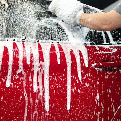 Foamy car wash. A red vehicle is lathered for cleaning with a mitt.