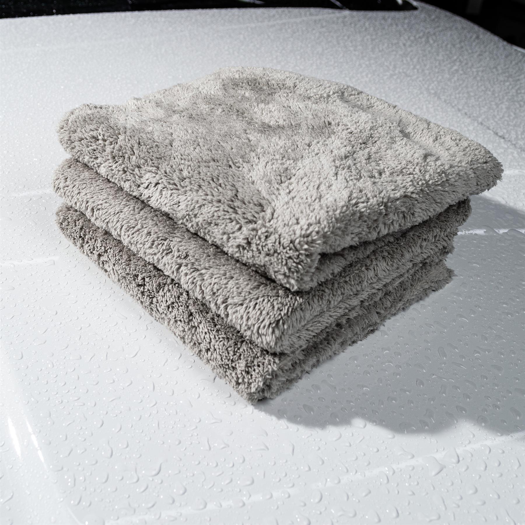 Stack of plush microfibre cloths on a wet white car bonnet. Ideal for Turtle Wax car care.
