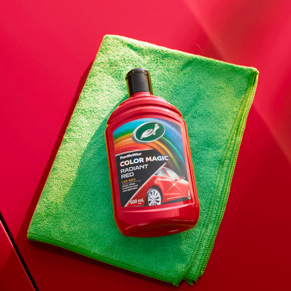 Turtle Wax Color Magic Radiant Red, a car wax, rests on a green microfibre cloth atop a red car panel, promising shine and restoration.
