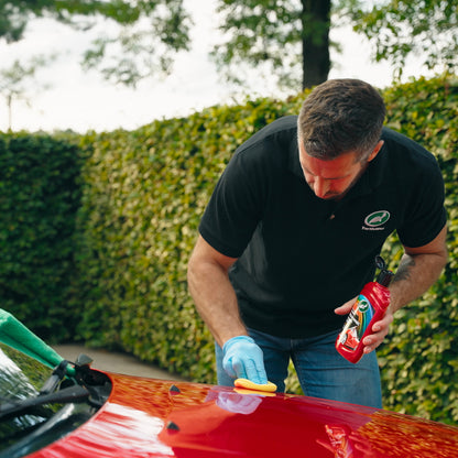 Man applying colour-enhancing Turtle Wax polish to a bright red car using a sponge. Car detailing.