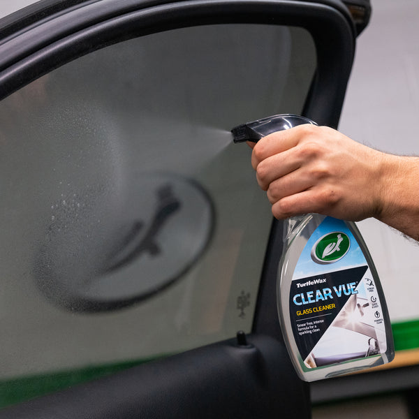 Close-up of Clear-Vue Glass Cleaner being applied to a car windshield with water droplets and reflections visible.
