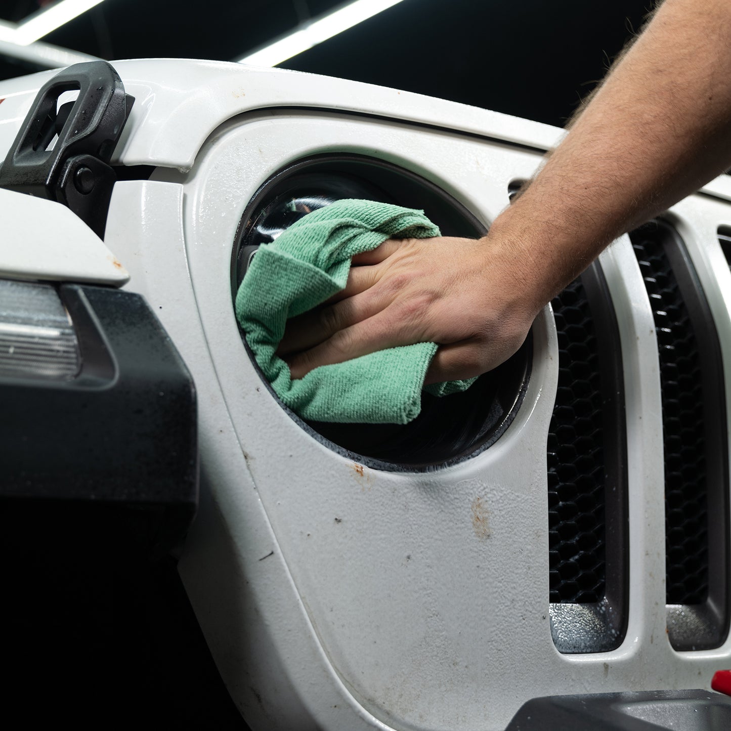 Detailing a white vehicle's headlight. Cleaning insect residue from the bodywork for a spotless, gleaming finish with a cloth.