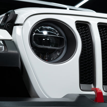 White SUV grill detail featuring honeycomb design, round headlight, and a red tow hook.