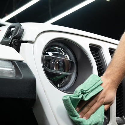 Cleaning a white SUV headlight with a microfibre cloth. Auto detailing, vehicle care.