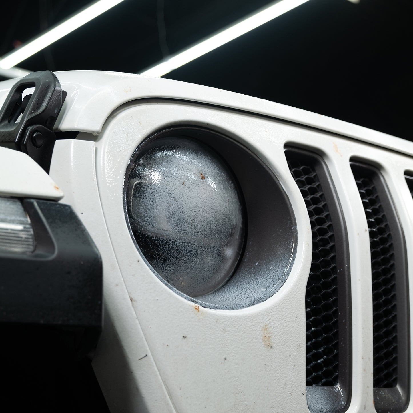 Close-up: White vehicle front, grille detail. Headlight covered in bug splats. Ideal for Turtle Wax Insect Remover advertising.