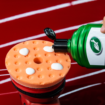 Turtle Wax application. Green bottle dispensing fluid onto a pad. Car care detailing on a red surface.
