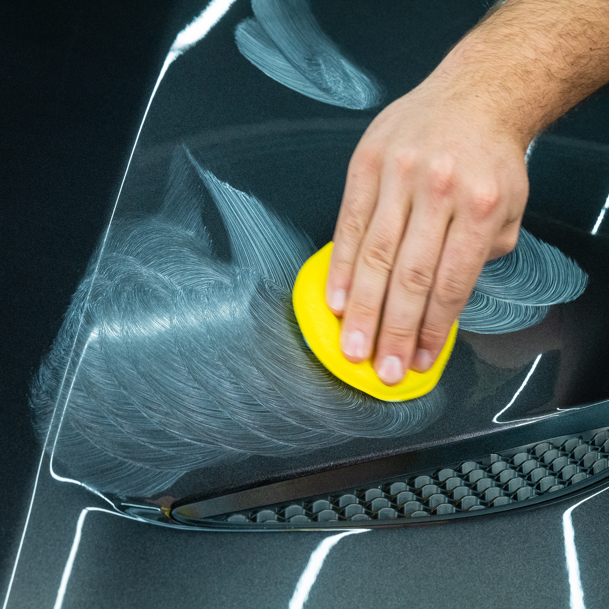 Man applying Turtle Wax to a black car bonnet. A yellow applicator pad is being used. Auto detailing, vehicle care concept.
