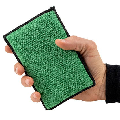 Hand holds a green, soft-textured interior cleaning pad with black edging, ready for car care.