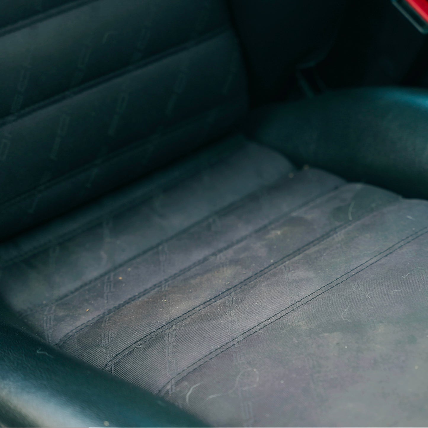 Close-up of a lightly soiled, dark, patterned cloth car seat interior. Showing the detail of the texture and stitching.