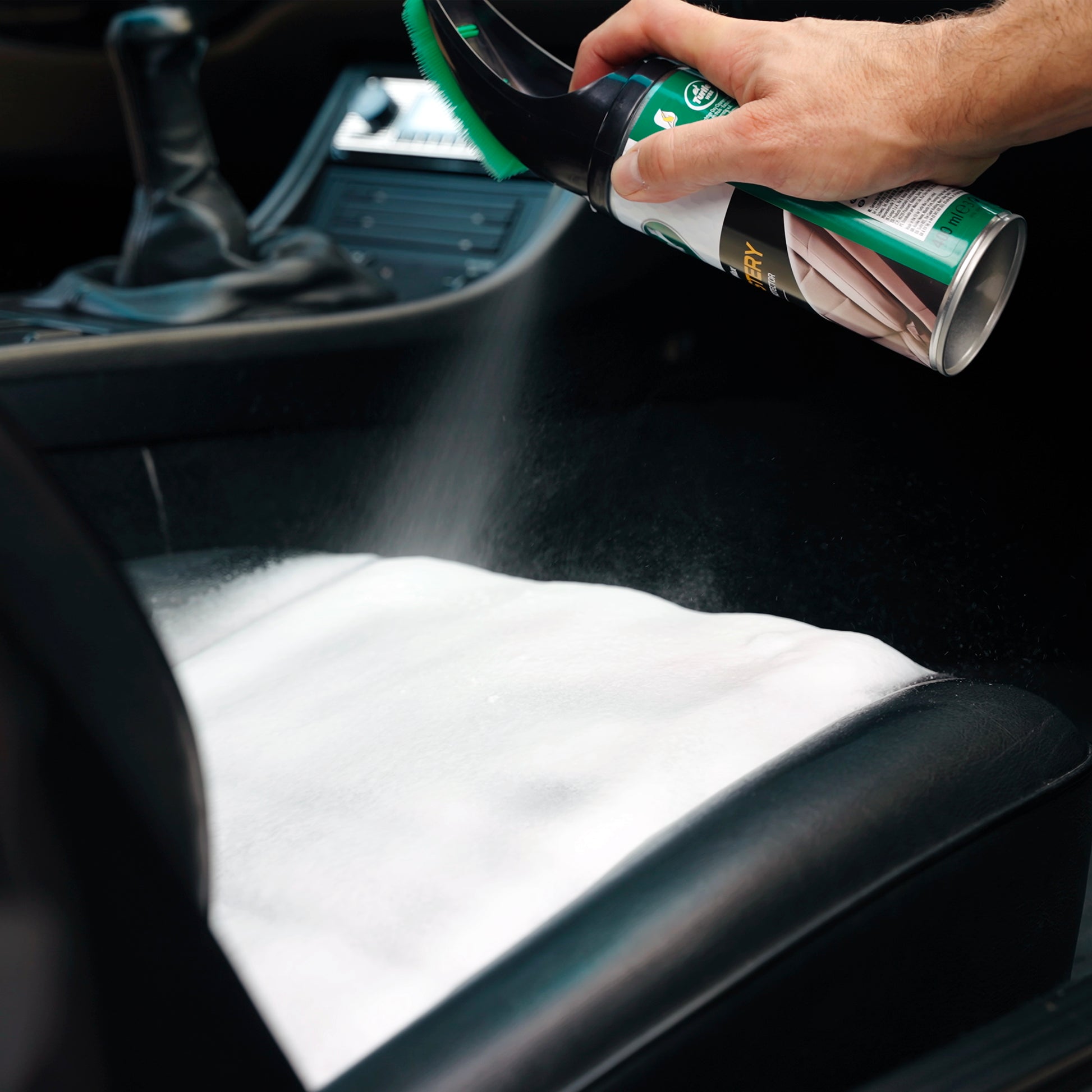 Turtle Wax upholstery cleaner with brush applying foam onto a black car seat. Interior detailing.
