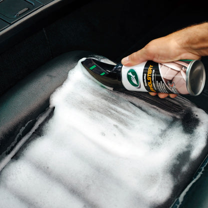 Cleaning a car's interior: Turtle Wax upholstery cleaner with brush applicator being used on a leather car seat.