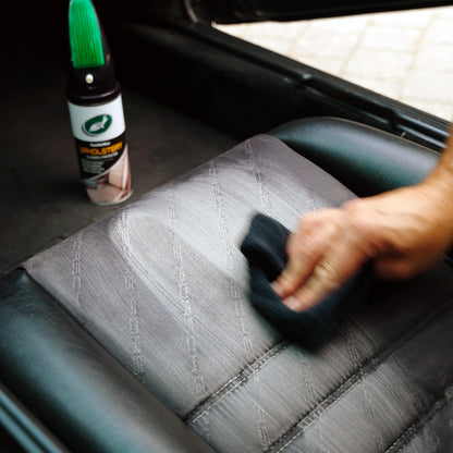 Car interior being cleaned. An upholstery product is visible in the background next to the seat. Detailing cloth being used. Turtle Wax can shown.