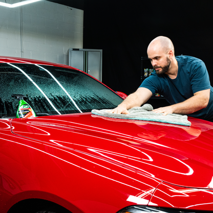 Man cleaning a wet, red car with a cloth. Turtle Wax spray bottle on the vehicle. Car detailing, auto maintenance.
